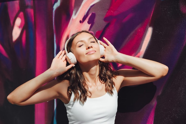 Een jonge gelukkige vrouw gekleed in een witte top en paarse rok koptelefoon luisteren naar muziek dansen op