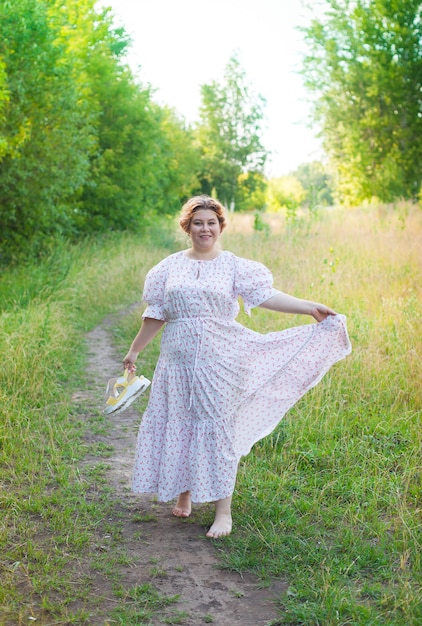 Een jonge gelukkige vrouw loopt op een zomerdag blootsvoets in een veld, met schoenen in haar handen. Model plus maat. selectieve aandacht.