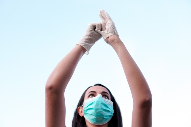 Een jonge gemaskerde vrouw die beschermende handschoenen aantrekt met de lucht op de achtergrond