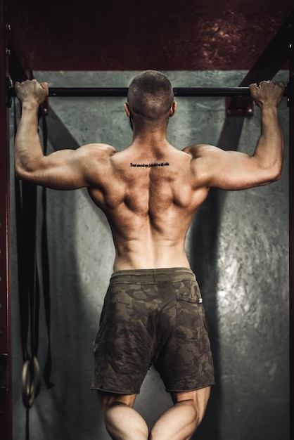 Een jonge gespierde bodybuilder man doet pull-up oefeningen in de sportschool.