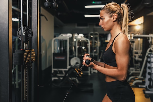 Een jonge gespierde vrouw doet training op een machine in de sportschool. Ze pompt haar bicepsspier met zwaar gewicht op.