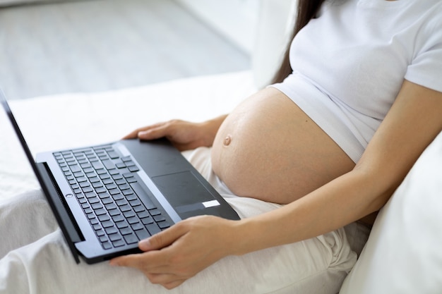 Een jonge gezonde zwangere vrouw in de late zwangerschap zit met een laptop