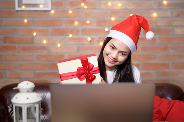 Een jonge glimlachende vrouw die rode Kerstmanhoed draagt die videogesprek voert op sociaal netwerk met familie en vrienden op eerste kerstdag.