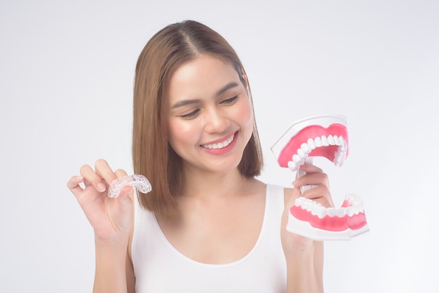 Een jonge glimlachende vrouw met invisalign beugels en kunstmatig tandmodel op wit, tandheelkundige gezondheidszorg en orthodontisch concept.