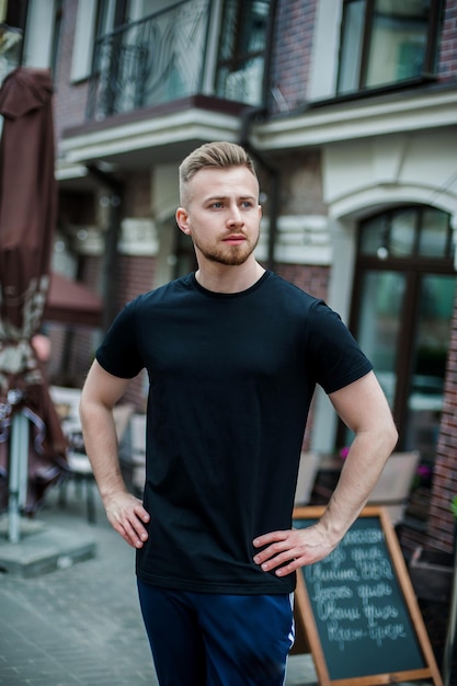 Een jonge hipster gekleed in een zwarte t-shirt staat bij het muurmodel voor een t-shirtdrukkerij