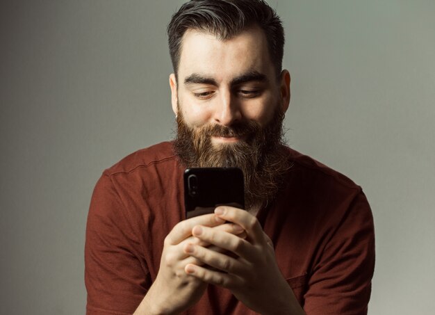 Een jonge hipster-stijl man met een baard en een modern kapsel glimlachen terwijl hij kijkt naar zijn telefoonscherm met kopie ruimte