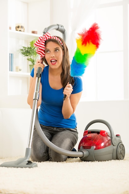 Een jonge huisvrouw geknield naast de stofzuiger met een stofdoek in de hand, tevreden met het goede werk om het huis op te ruimen.