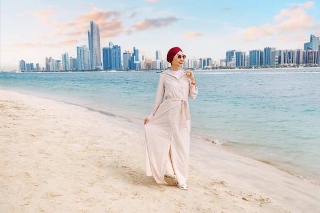 Een jonge Indiase vrouw loopt langs het strand en geniet van het adembenemende uitzicht op de zee van de torenhoge wolkenkrabbers van Abu Dhabi