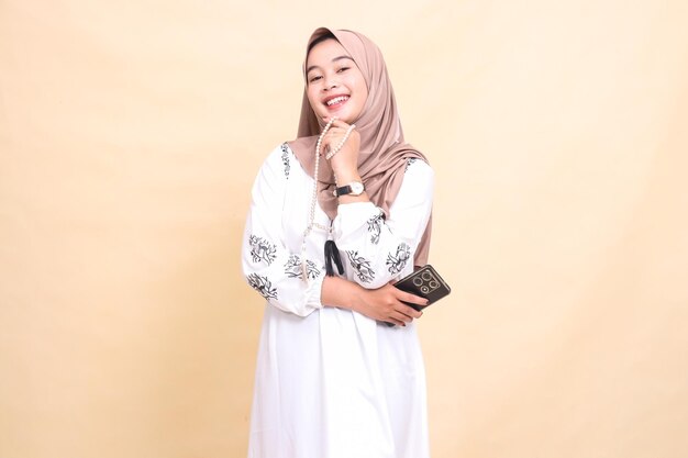 een jonge Indonesische moslimvrouw met een hijab glimlacht vrolijk met gebedskralen in haar hand en brengt een