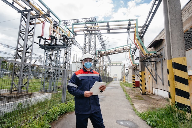 Een jonge ingenieur staat in een masker op een elektrisch onderstation.