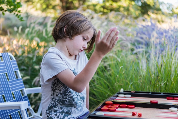 Een jonge jongen die buiten backgammon speelt in een tuin