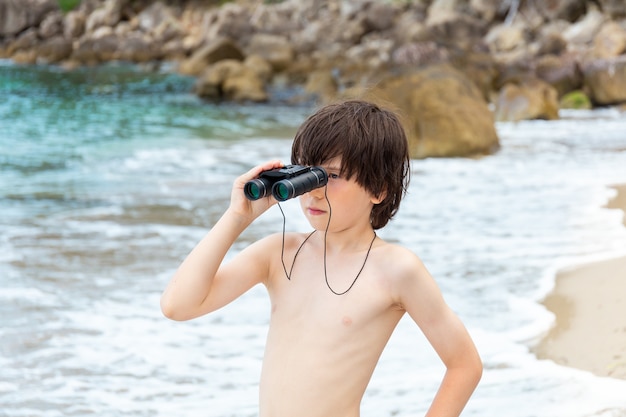 Een jonge jongen die door een verrekijker kijkt die aan de kust op het strand verblijft.