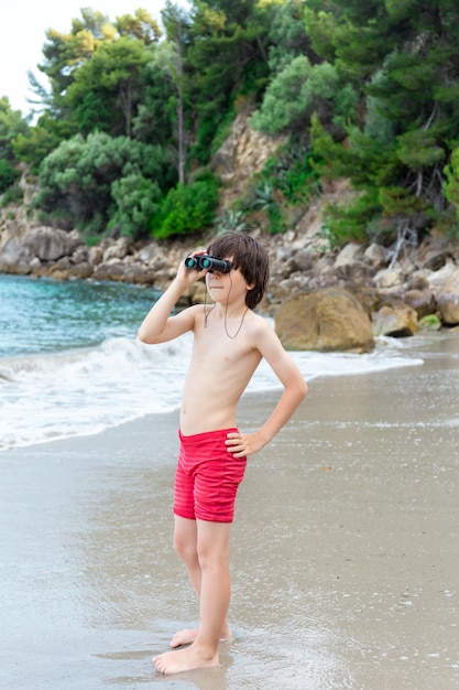 Een jonge jongen die door een verrekijker kijkt die aan de kust op het strand verblijft.