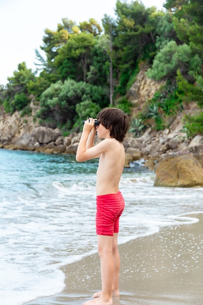 Een jonge jongen die door een verrekijker kijkt die aan de kust op het strand verblijft.