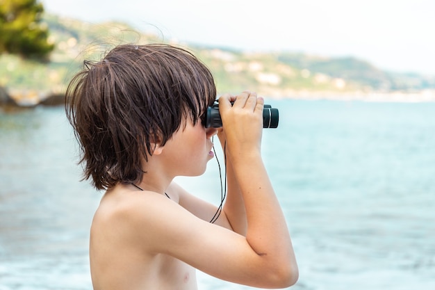 Een jonge jongen die door een verrekijker kijkt die aan de kust op het strand verblijft.