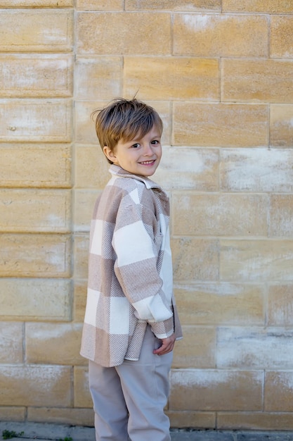 Foto een jonge jongen die een trui en een sjaal draagt staat op een stenen muur