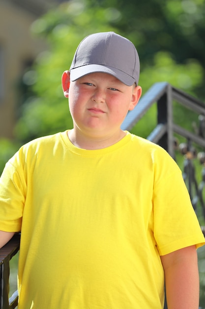 Een jonge jongen in een geel T-shirt en pet en zonnebril staat in de natuur. Hoge kwaliteit foto