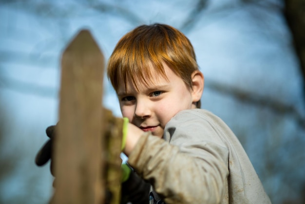 Een jonge jongen in het dorp bereidt zich voor om in de tuin te werken. Hij draagt rubberen handschoenen die zich aan een houten hek vasthouden