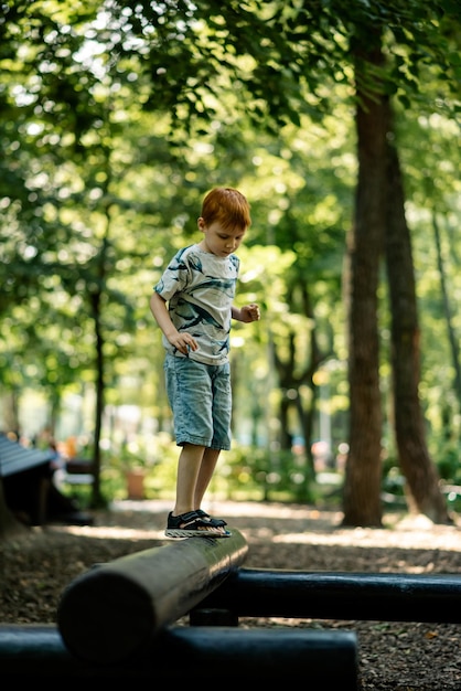 Foto een jonge jongen loopt op een boomstam op de speelplaats actieve zomervakantie