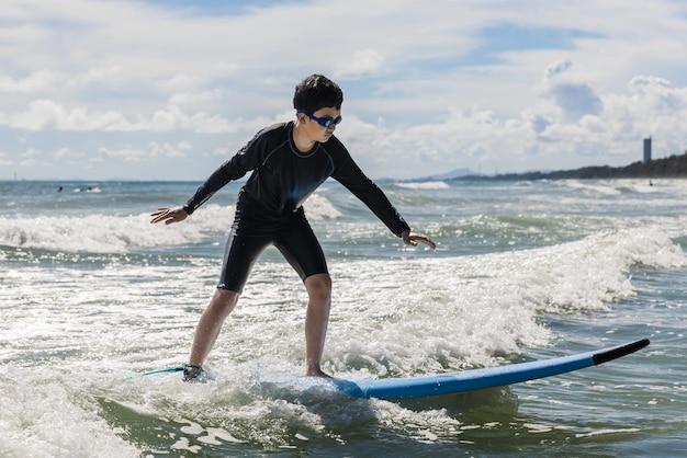 Foto een jonge jongen met een zwembril staat op een zacht bord terwijl hij aan het surfen is in een beginnersklasse