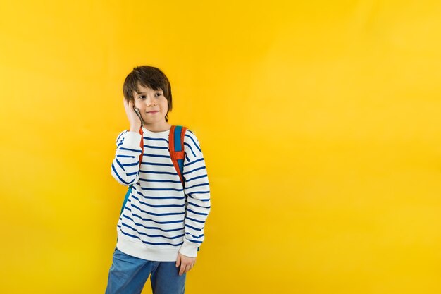 Een jonge jongen van negen jaar oud met een rugzak op zijn schouders die op zijn smartphone praat met zijn ouders of vrienden