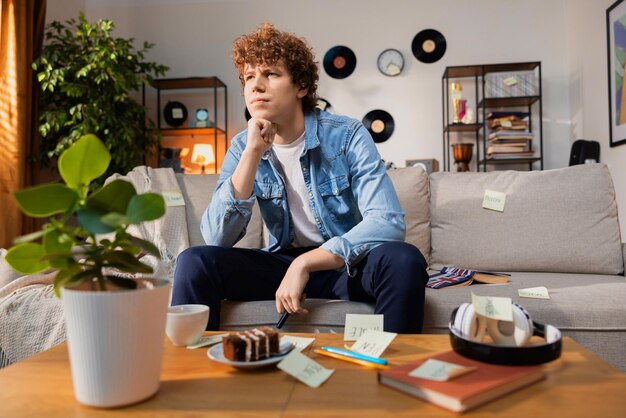 Foto een jonge jongen zit peinzend op een canpa met een tafel voor hem man kijkt alert vooruit