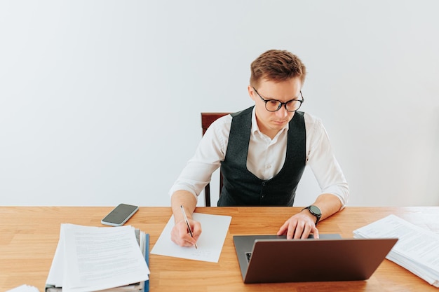 Een jonge kantoormedewerker is druk bezig met schrijven op papier terwijl hij een bril draagt in zijn modern