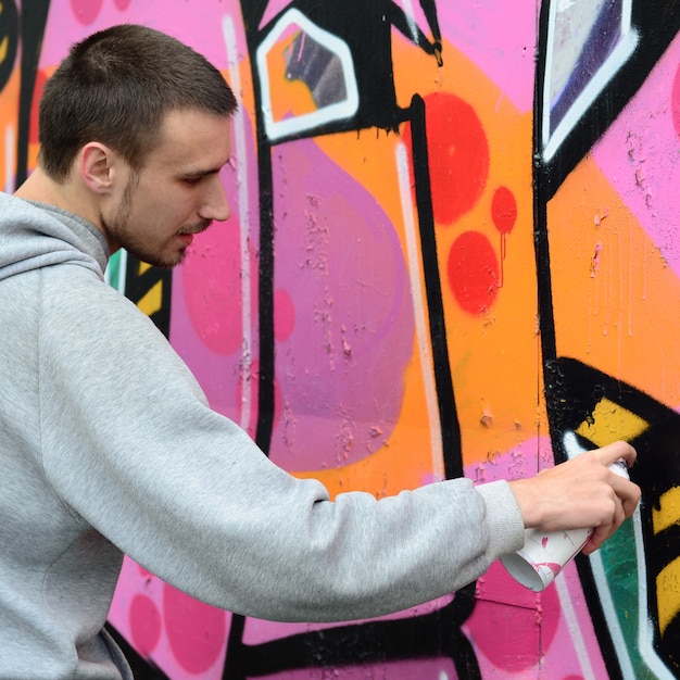 Een jonge kerel in een grijze hoodie schildert graffiti in roze en groen c