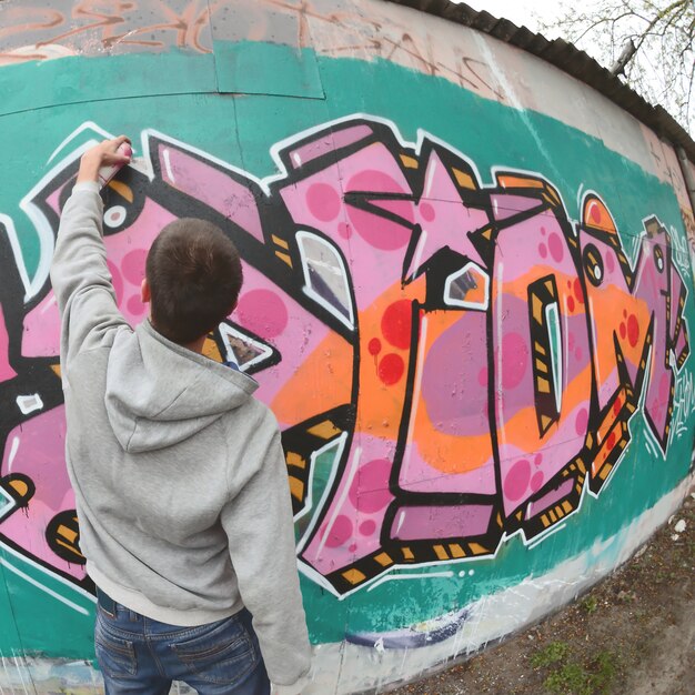 Een jonge kerel in een grijze hoodie schildert graffiti