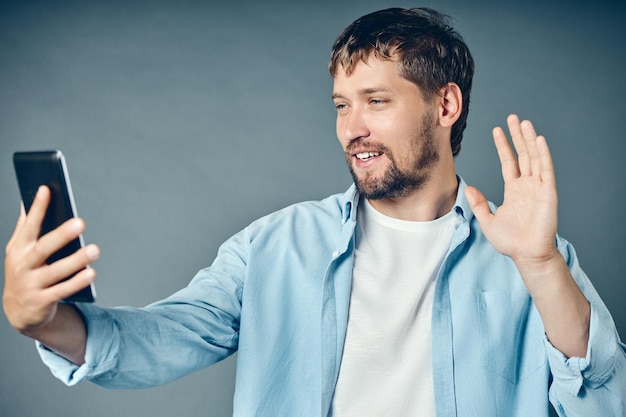 Een jonge kerel lacht en stuurt groeten op internet met behulp van een smartphone of tablet moderne communicatiemiddelen