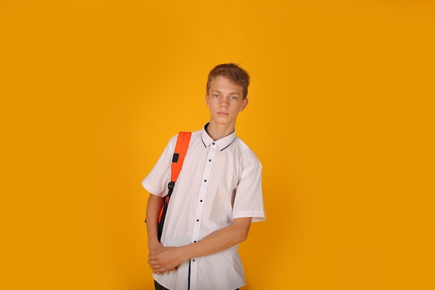 Een jonge knappe man in een wit overhemd met een oranje rugzak op zijn schouders gele achtergrond