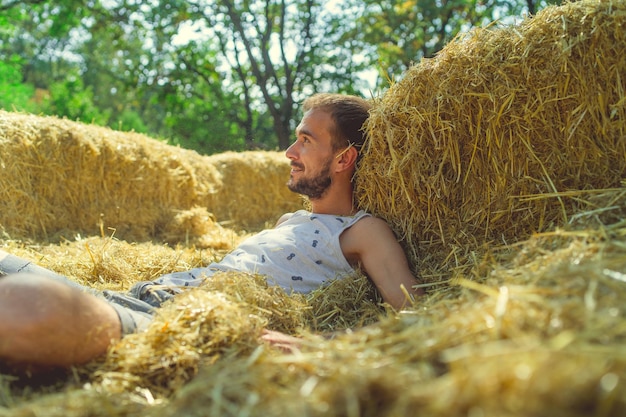 Een jonge knappe man met een slank gebouwde baard in een t-shirt en korte broek ligt op een zonnige dag in het hooi