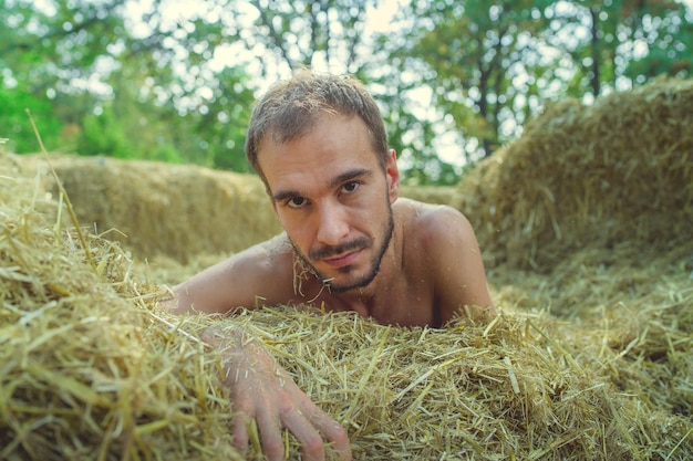 Een jonge knappe man met een slank gebouwde baard in een t-shirt en korte broek ligt op een zonnige dag in het hooi