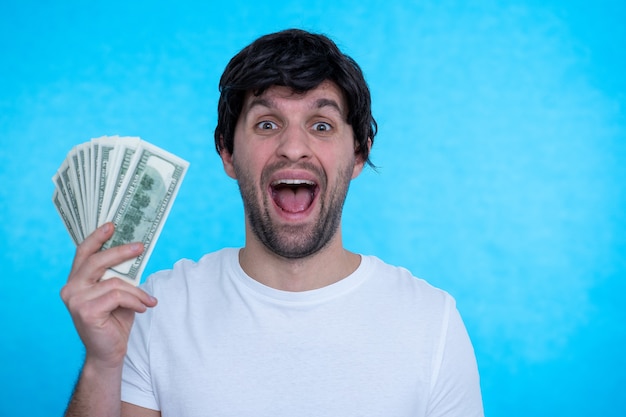 Een jonge knappe zelfverzekerde man houdt gelukkig dollars in zijn handen