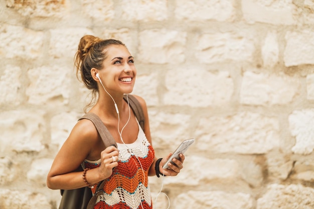 Een jonge lachende vrouw die van muziek geniet tijdens het verkennen van een mediterrane stad tijdens een zomervakantie.