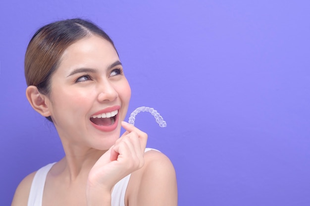 Een jonge lachende vrouw met invisalign beugels in de studio, tandheelkundige gezondheidszorg en orthodontisch concept.