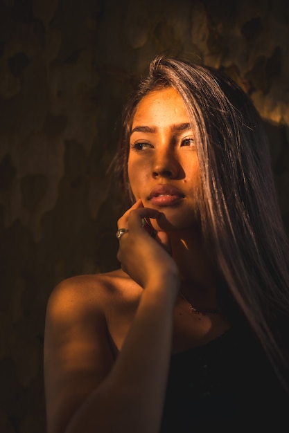 Een jonge Latina brunette leunt tegen een boom met een klein licht op haar gezicht. Portret met een zoete en sensuele uitstraling