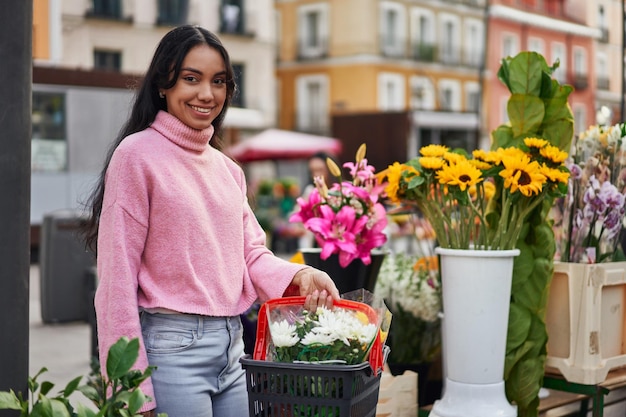 Een jonge Latina-vrouw die planten koopt met een mand vol planten in een bloemistenwinkel op straat