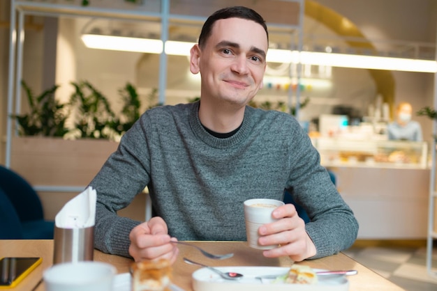 Een jonge man aan het ontbijt en glimlachend kijkend naar de camera in een café