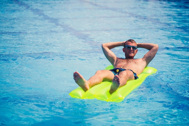 Een jonge man baadt in het zwembad op een gele opblaasbare matras Ontspan in de felle zon op vakantie Gelukkig succesvolle kerel