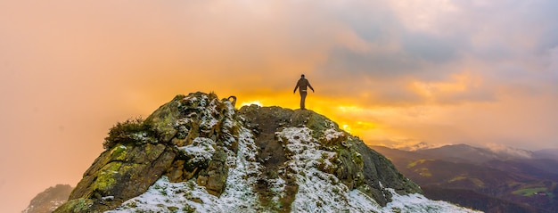 Een jonge man bovenop de berg in de besneeuwde winteroranje zonsondergang, op de berg Peñas de Aya in de stad Oiartzun bij San Sebastian, Spanje