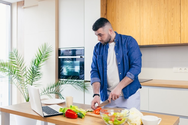 Een jonge man brengt een dag thuis door en bereidt een ontbijt met groenten in de keuken