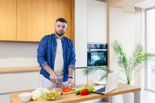 Een jonge man brengt een dag thuis door en bereidt een ontbijt met groenten in de keuken