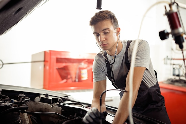 Een jonge man controleert de motor van een auto.