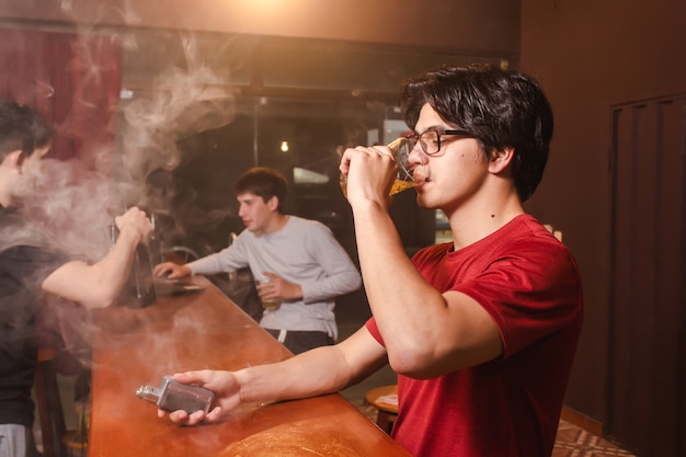 Een jonge man die bier drinkt en dampt met zijn vrienden aan de bar.