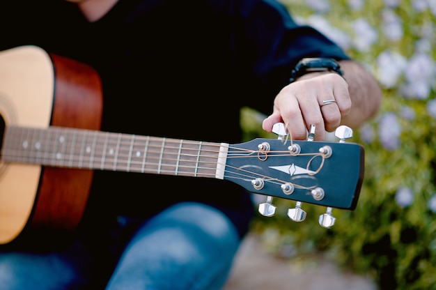 een jonge man die een gitaar speelt terwijl hij in een natuurlijke tuin zit