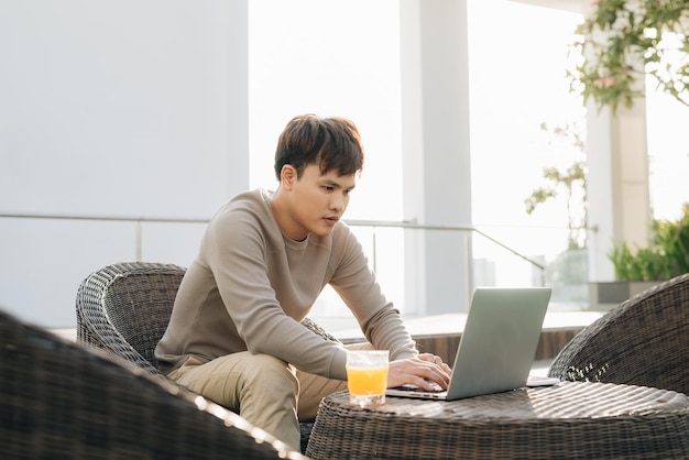 Een jonge man die een laptop gebruikt terwijl hij buiten op een bank zit