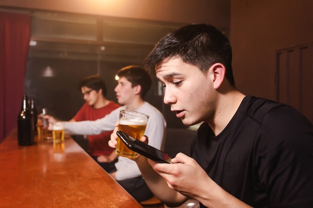 Een jonge man die een spraakaudio stuurt terwijl hij een biertje drinkt met zijn vrienden aan de bar.