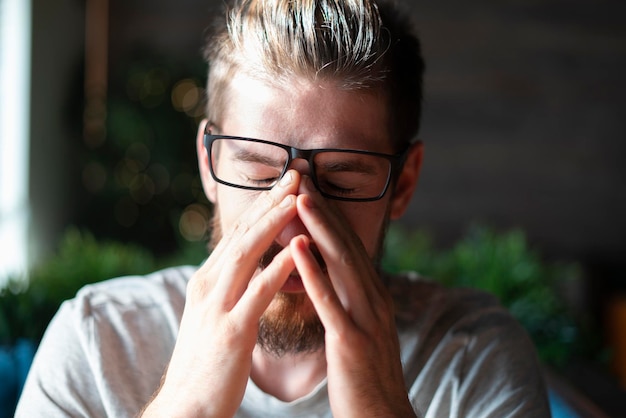 Een jonge man die ogen aanraakt, moe met een bril op