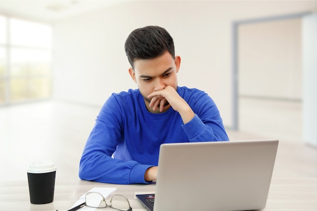 Een jonge man die op een laptop werkt. hij is boos en moe. op wit geïsoleerd